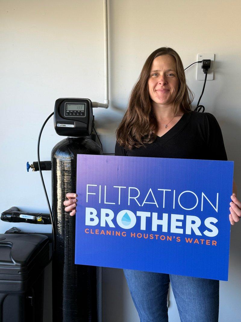 Happy customer holding Filtration Brothers sign next to water softener installation