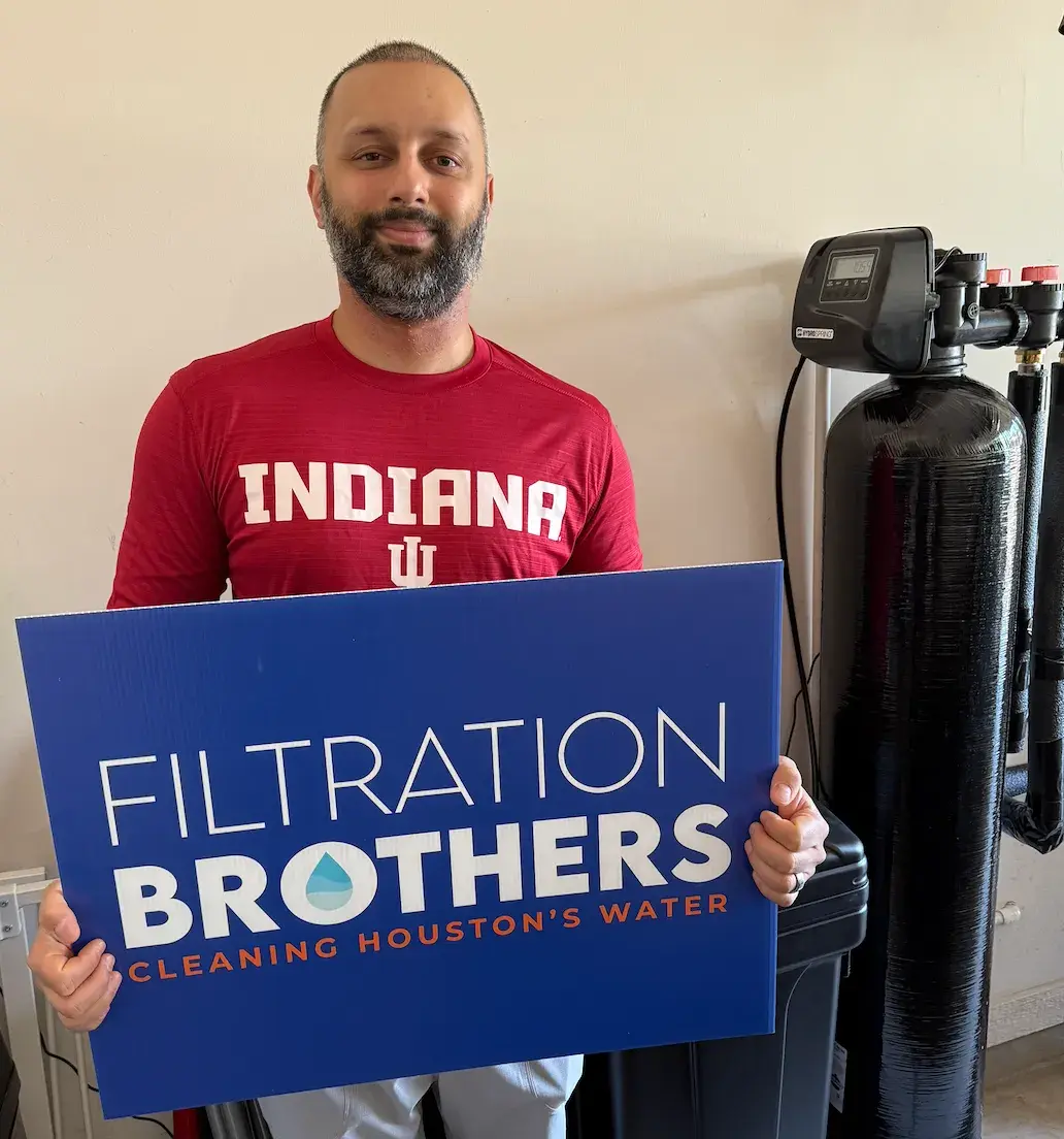 Happy customer holding Filtration Brothers sign next to water treatment system